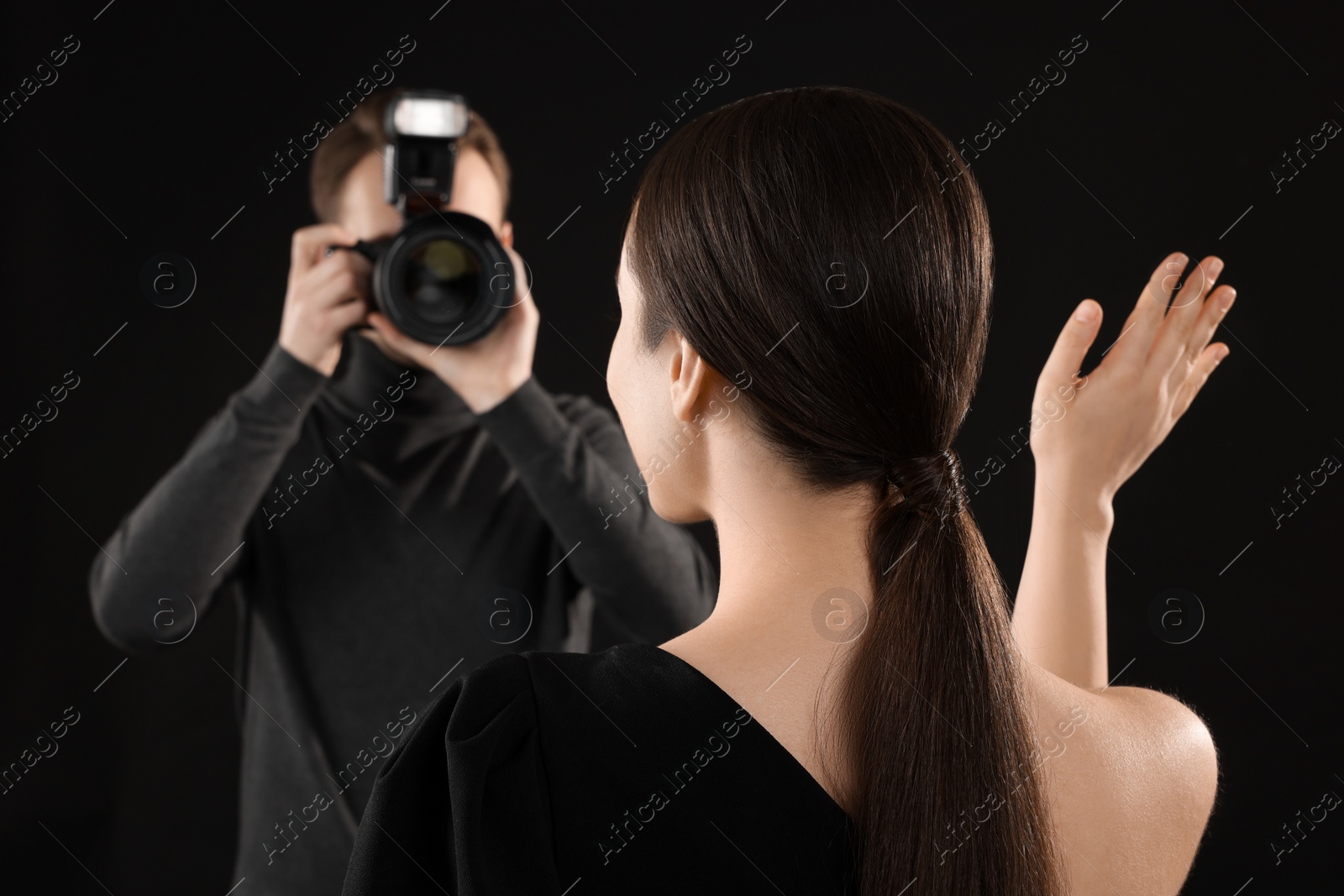 Photo of Photographer taking picture of model on black background, selective focus