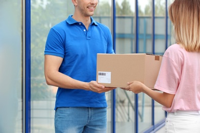 Young woman receiving parcel from courier outdoors. Delivery service