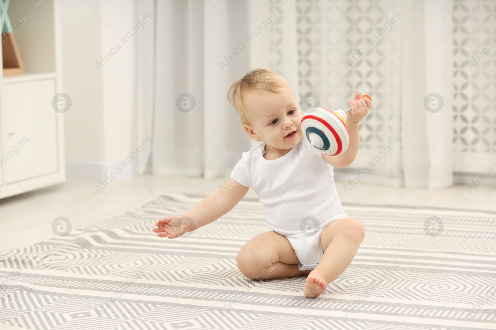 Photo of Children toys. Cute little boy playing with spinning top on rug at home