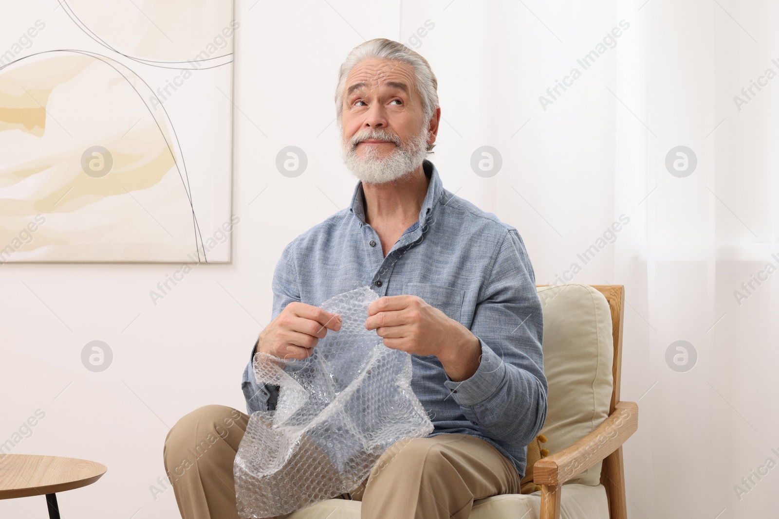 Photo of Happy senior man popping bubble at home. Stress relief