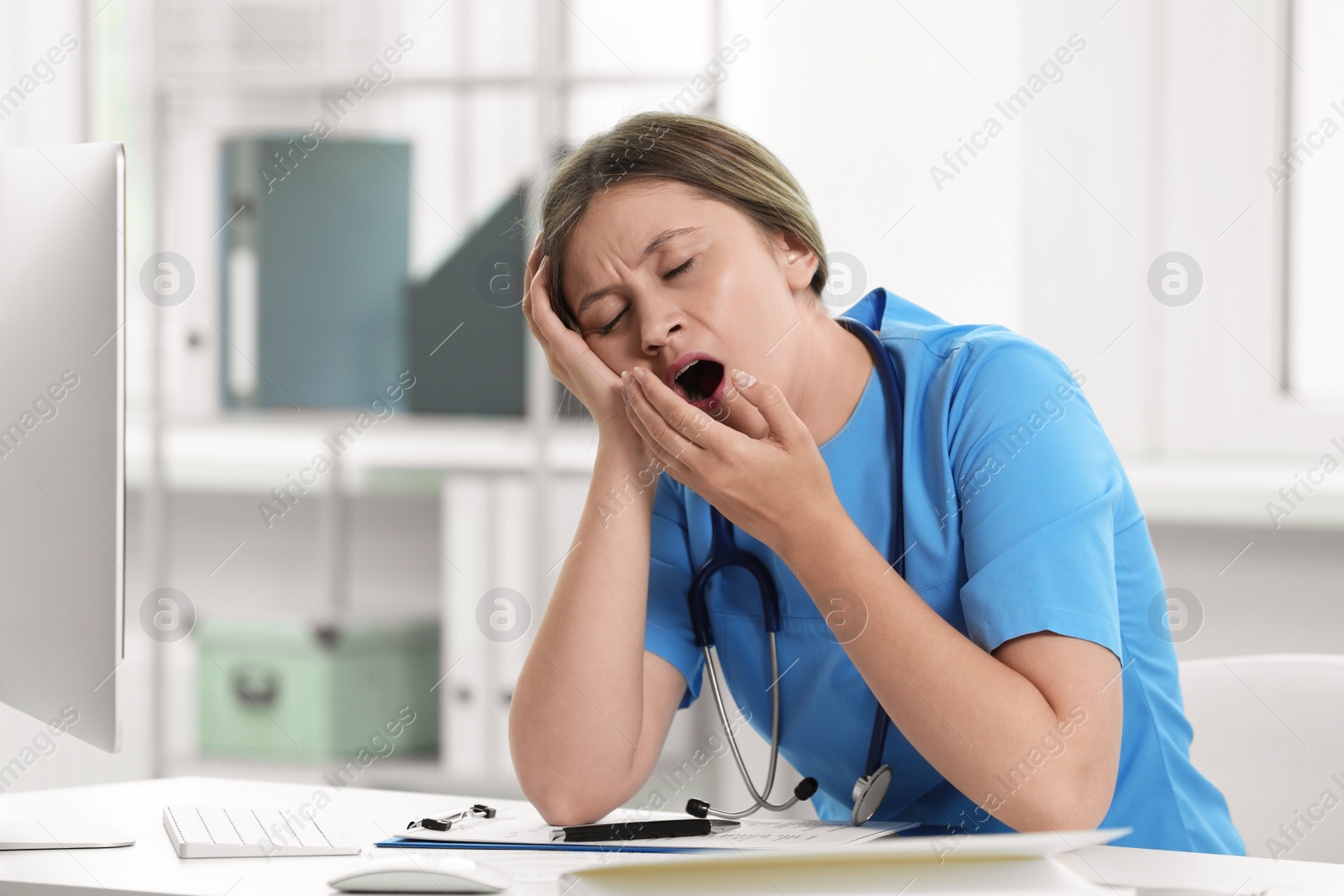 Photo of Exhausted doctor yawning at workplace in hospital