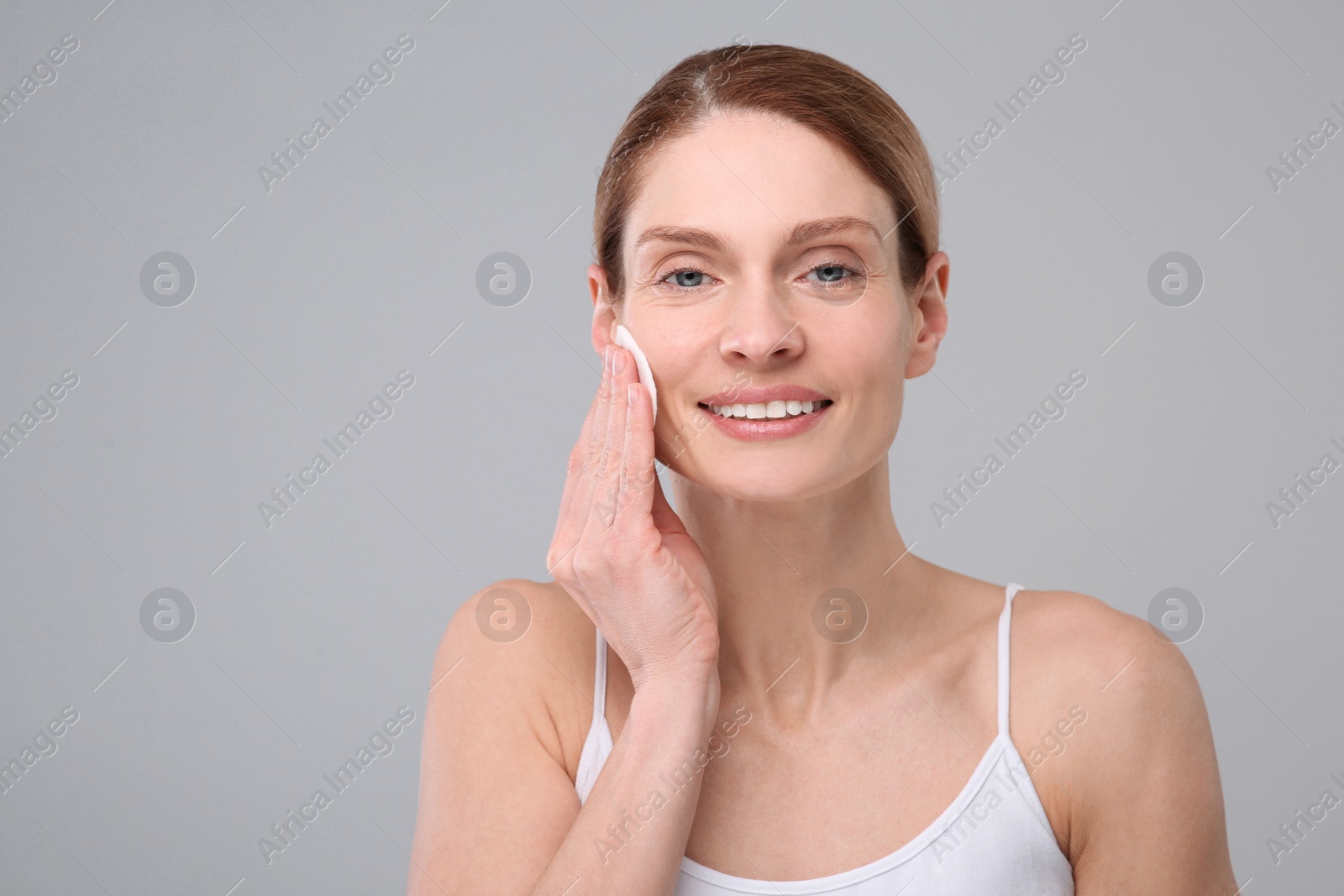 Photo of Beautiful woman removing makeup with cotton pad on gray background, space for text