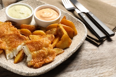 Photo of Plate with British traditional fish and potato chips on wooden table, closeup