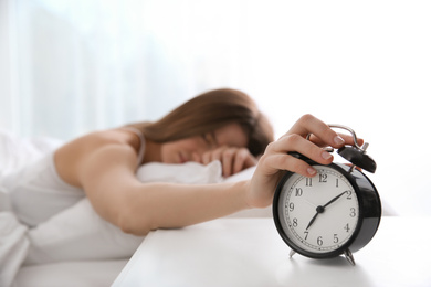 Photo of Young woman turning off alarm clock at home in morning, focus on hand