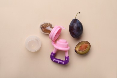 Photo of Nibbler with fresh plum on beige background, flat lay. Baby feeder