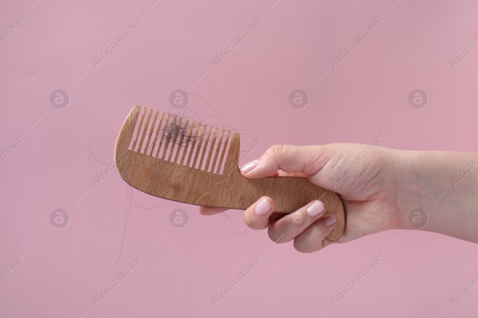 Photo of Woman holding comb with lost hair on pink background, closeup