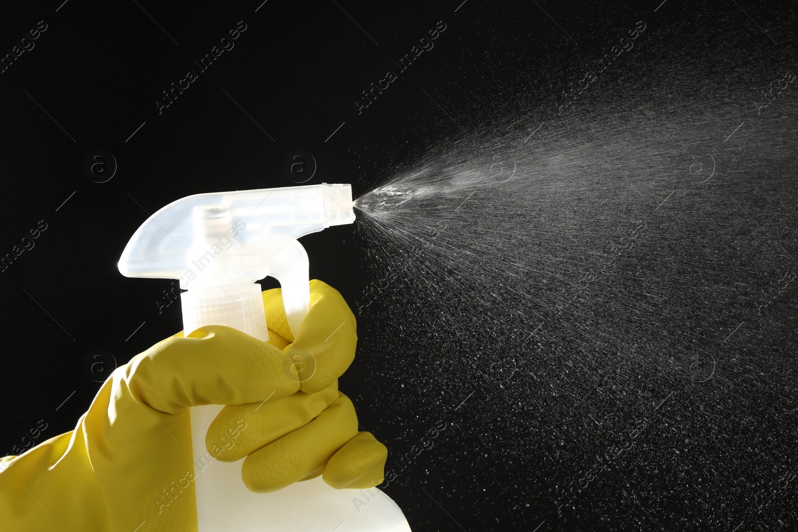 Photo of Woman spraying liquid from bottle on black background, closeup