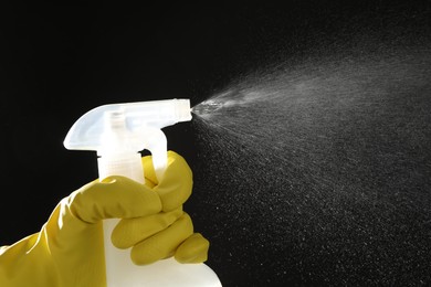 Photo of Woman spraying liquid from bottle on black background, closeup