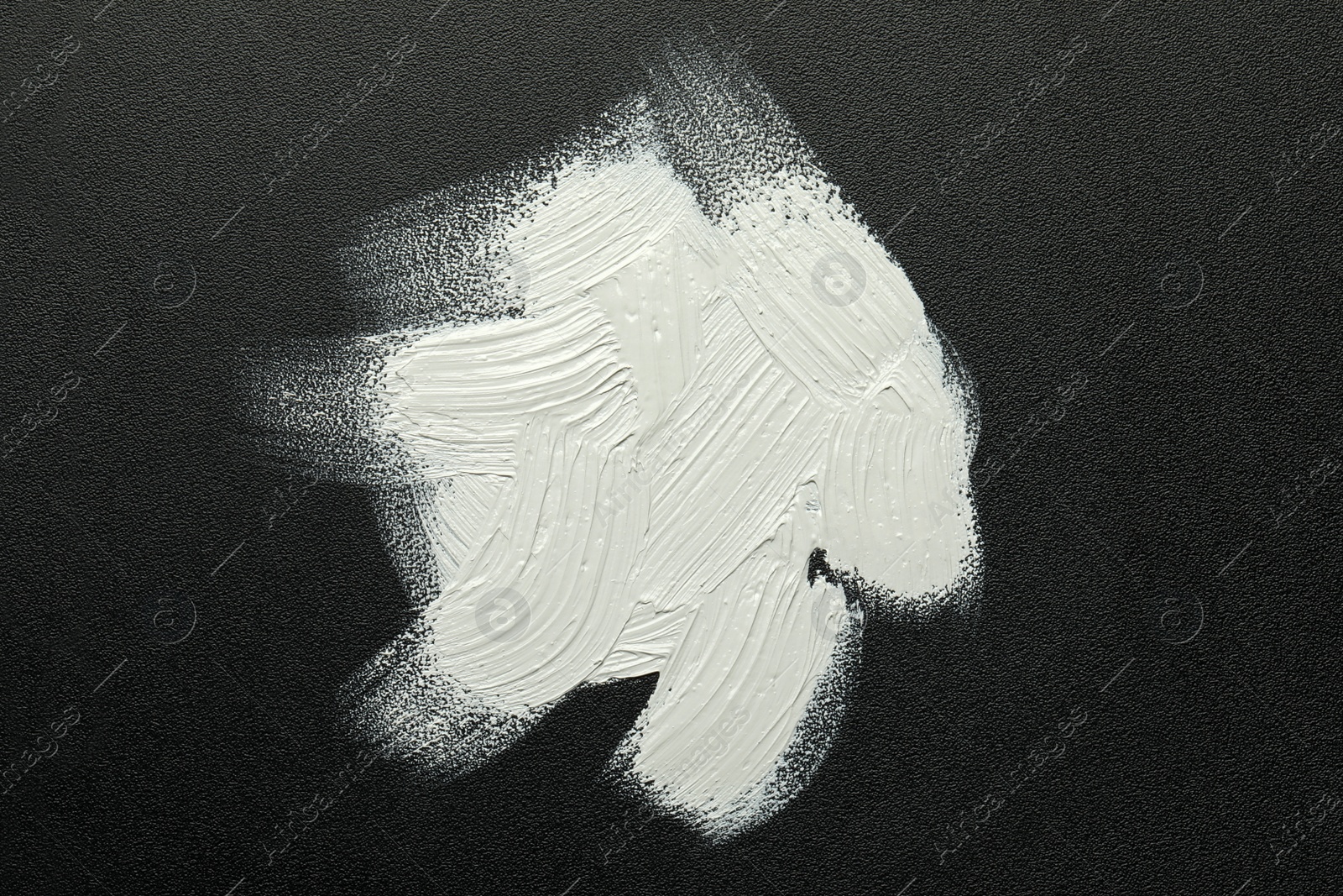 Photo of Strokes of white oil paint on black canvas, top view