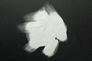 Photo of Strokes of white oil paint on black canvas, top view