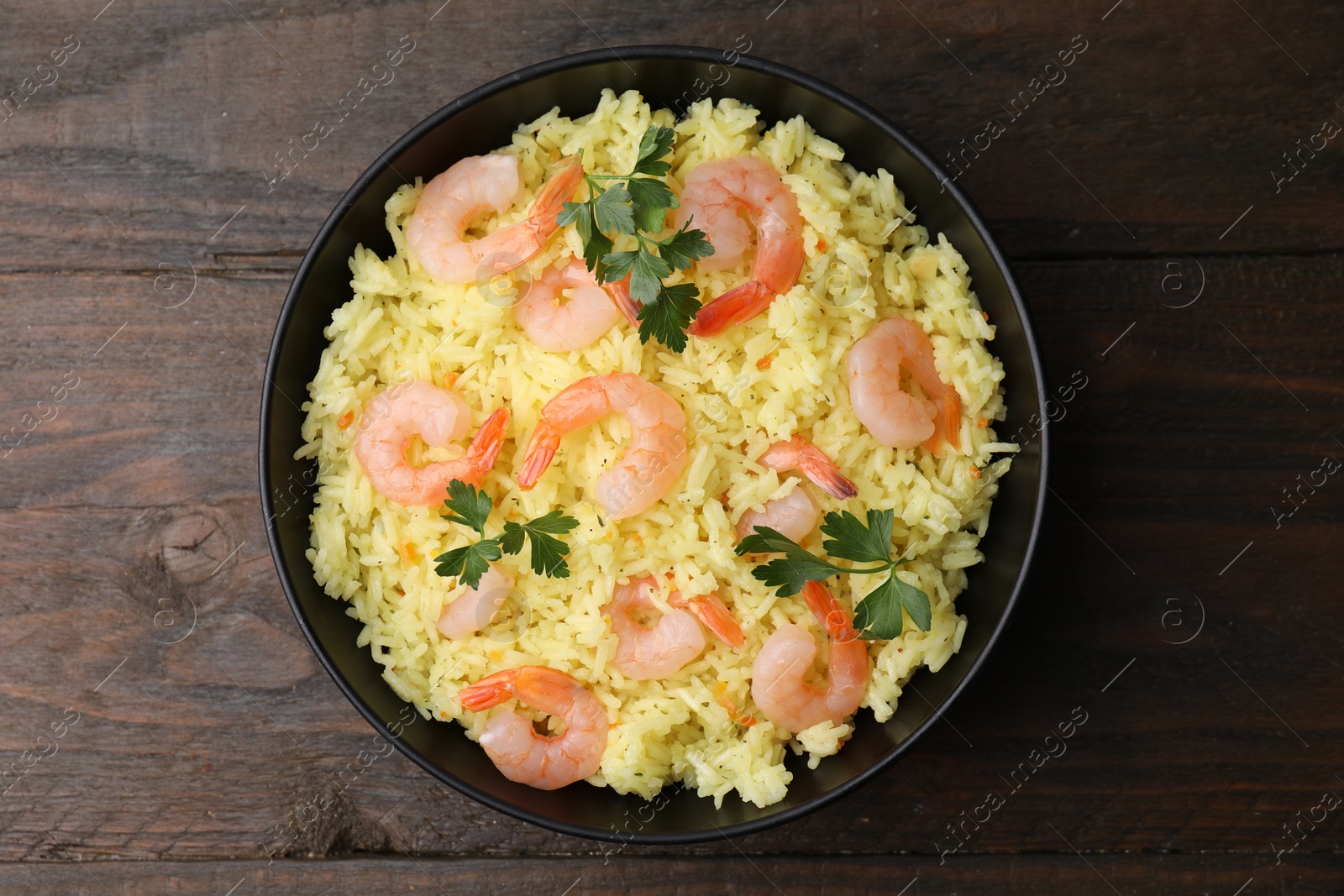 Photo of Delicious risotto with shrimps and parsley in bowl on wooden table, top view