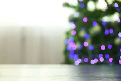 Photo of Blurred view of fir tree with glowing Christmas lights near table indoors