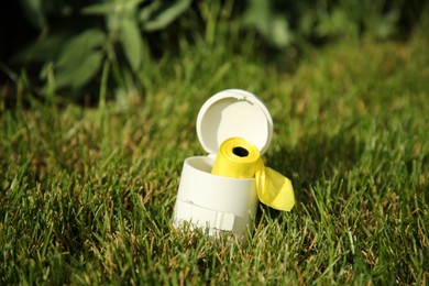 Holder with dog waste bags in green grass on sunny day