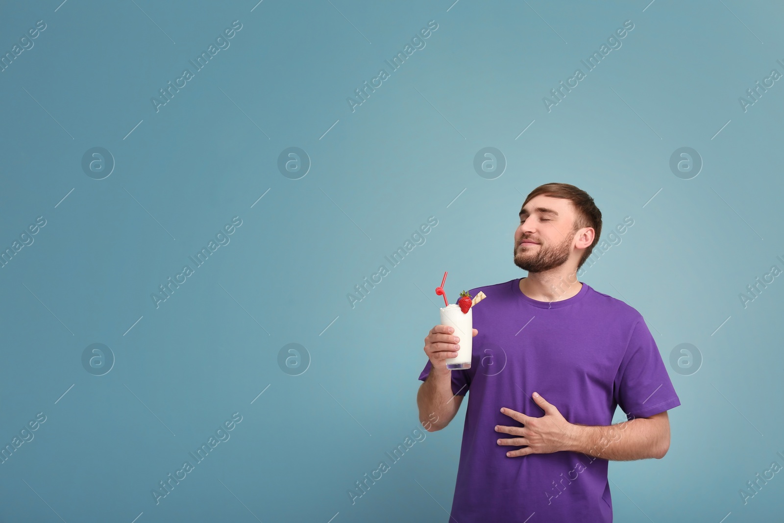 Photo of Young man with glass of delicious milk shake on color background