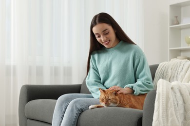 Photo of Beautiful woman petting cute cat on sofa at home, space for text
