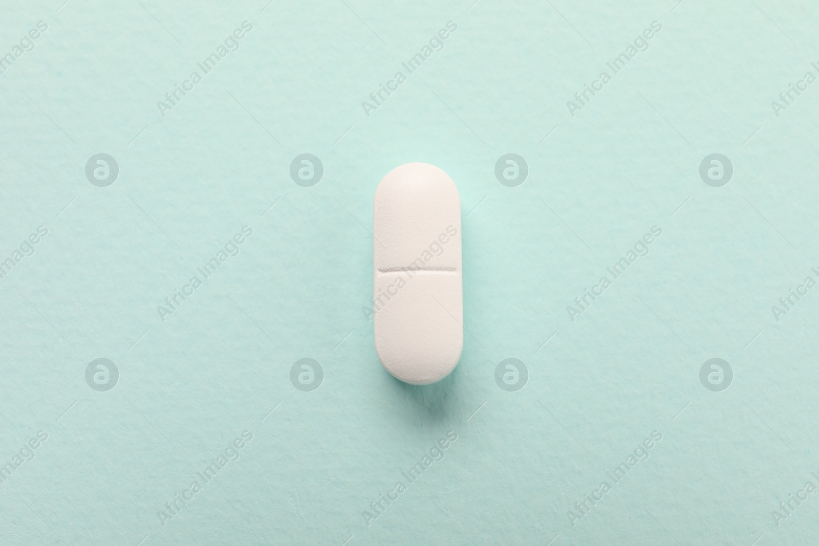 Photo of One white pill on mint background, top view