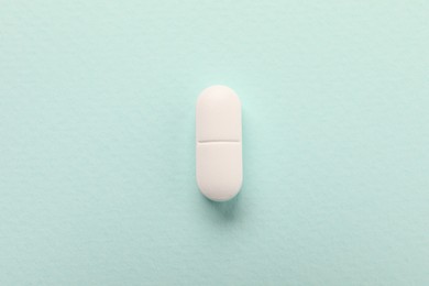 One white pill on mint background, top view