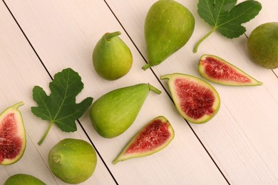 Cut and whole green figs with leaves on white wooden table, flat lay