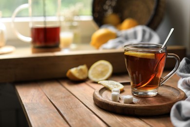 Photo of Glass cup with delicious tea, sugar and lemon on wooden table, space for text