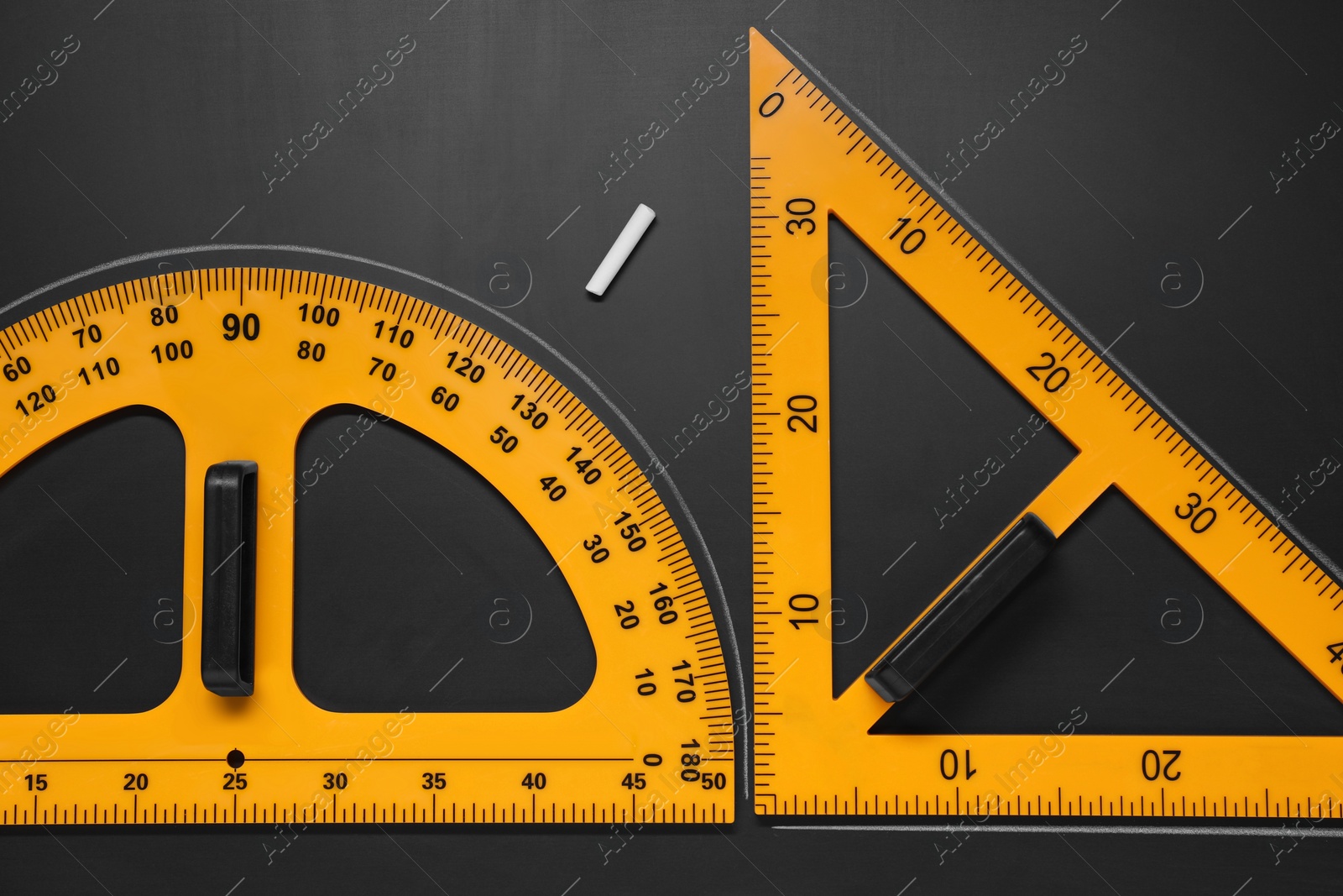 Photo of Protractor, triangle ruler and chalk on black table, flat lay