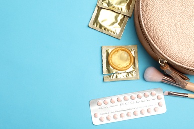 Photo of Flat lay composition with birth control pills and condoms on light blue background, space for text. Safe sex concept