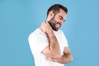 Photo of Young man scratching neck on color background. Allergies symptoms