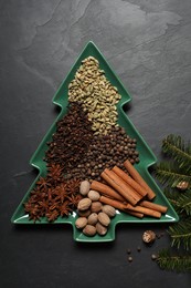 Photo of Different spices, nuts and fir branches on dark gray textured table, flat lay