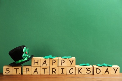 Photo of Leprechaun hat, clover leaves and wooden cubes with words Happy St Patrick's Day on table against green background, space for text