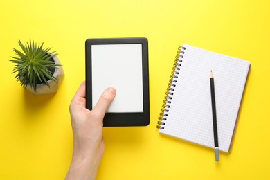 Photo of Woman using e-book reader on yellow background, top view