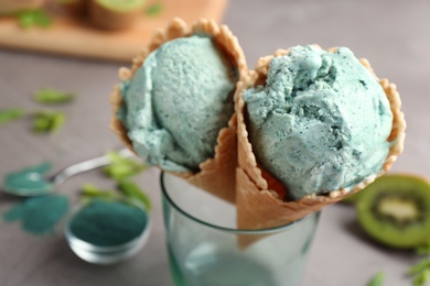Photo of Delicious spirulina ice cream cones in glass on table, closeup