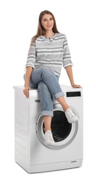 Photo of Young woman sitting on washing machine against white background. Laundry equipment