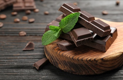 Photo of Pieces of dark chocolate with mint on wooden table