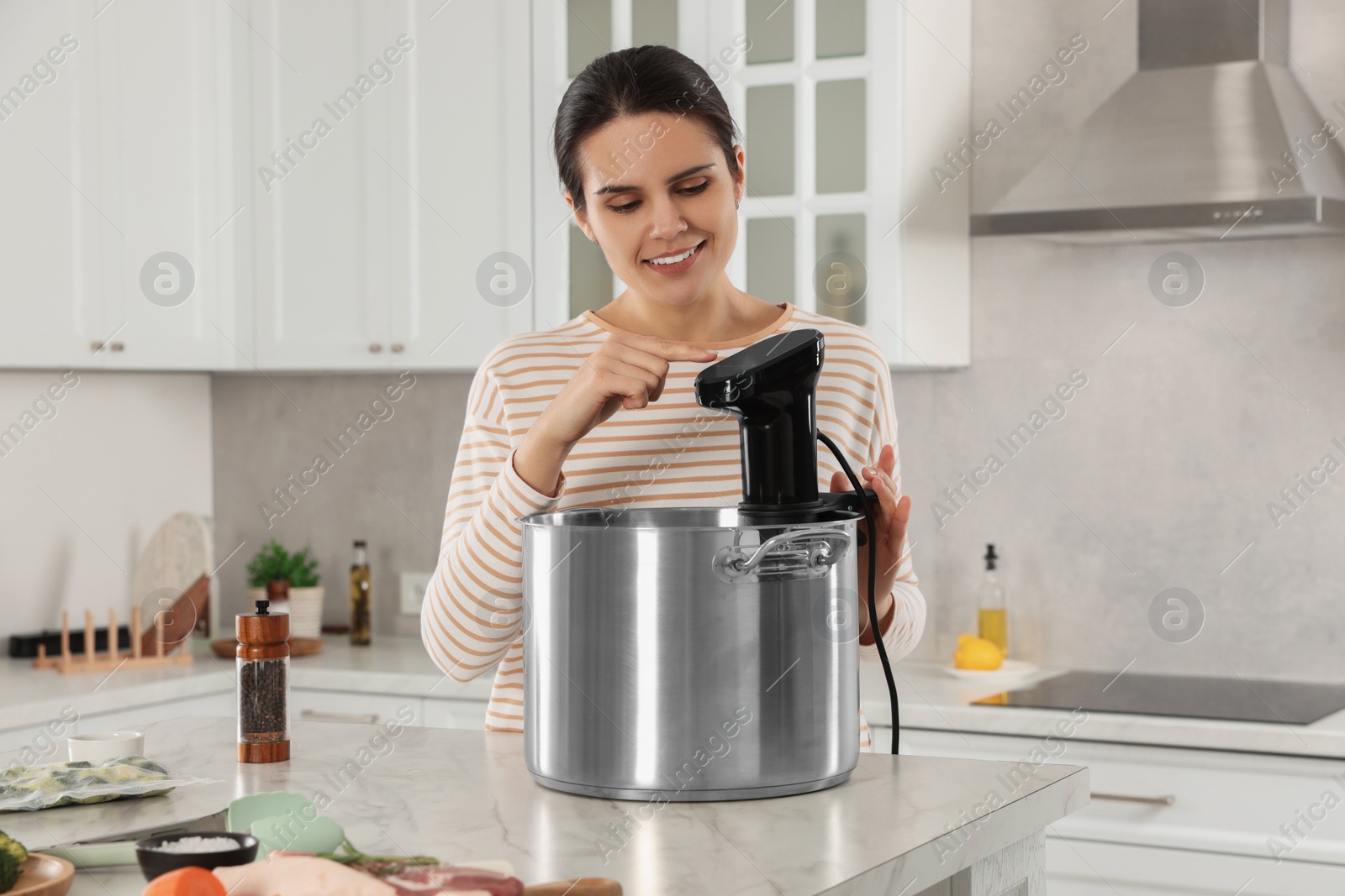 Photo of Woman using thermal immersion circulator at table in kitchen. Sous vide cooking