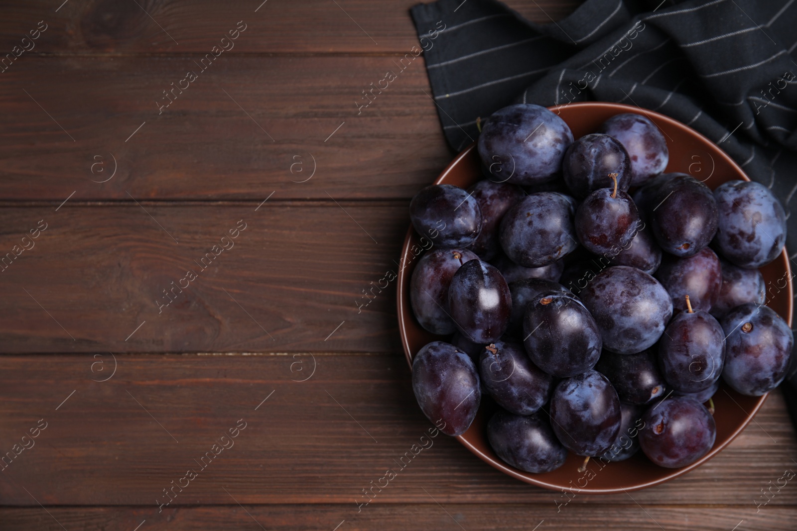 Photo of Delicious ripe plums in bowl on wooden table, top view. Space for text