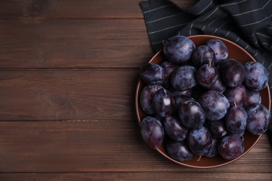 Photo of Delicious ripe plums in bowl on wooden table, top view. Space for text