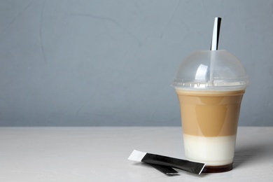 Plastic cup of tasty caramel macchiato on table, space for text