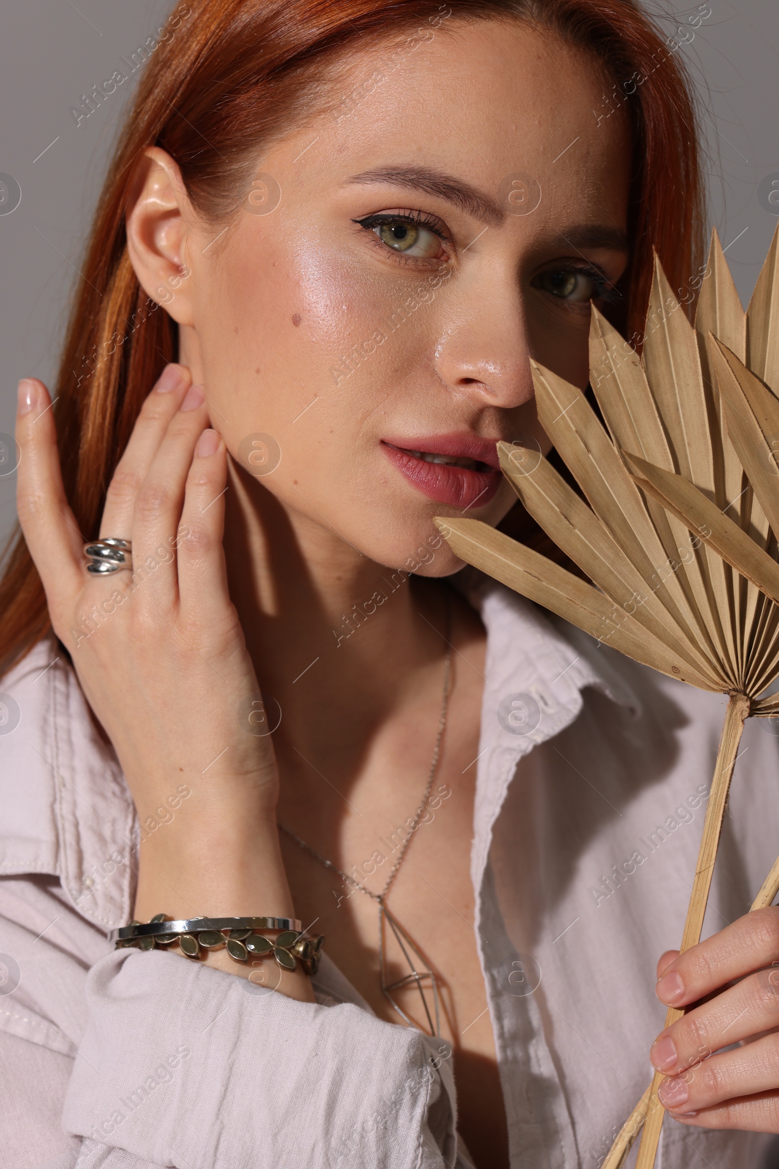 Photo of Beautiful young woman with elegant jewelry and decorative leaves on gray background