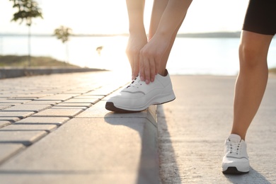 Young woman tying laces outdoors in morning, closeup