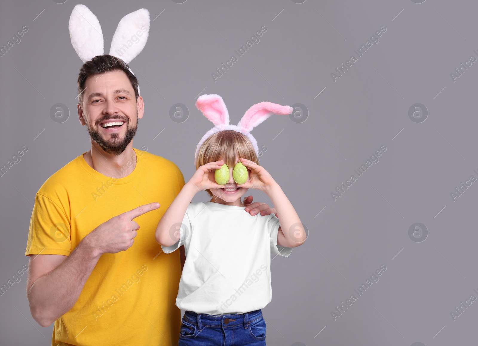 Photo of Father and son in bunny ears headbands having fun on grey background, space for text. Easter celebration