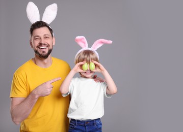 Photo of Father and son in bunny ears headbands having fun on grey background, space for text. Easter celebration