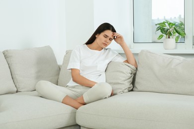 Photo of Young woman suffering from headache on sofa at home. Hormonal disorders