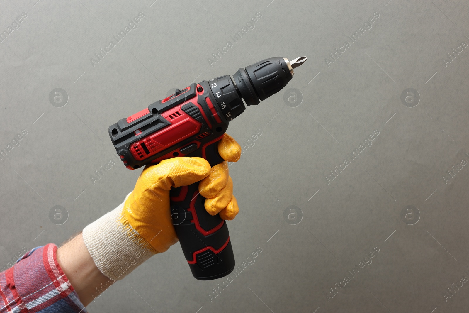 Photo of Handyman holding electric screwdriver on grey background, closeup