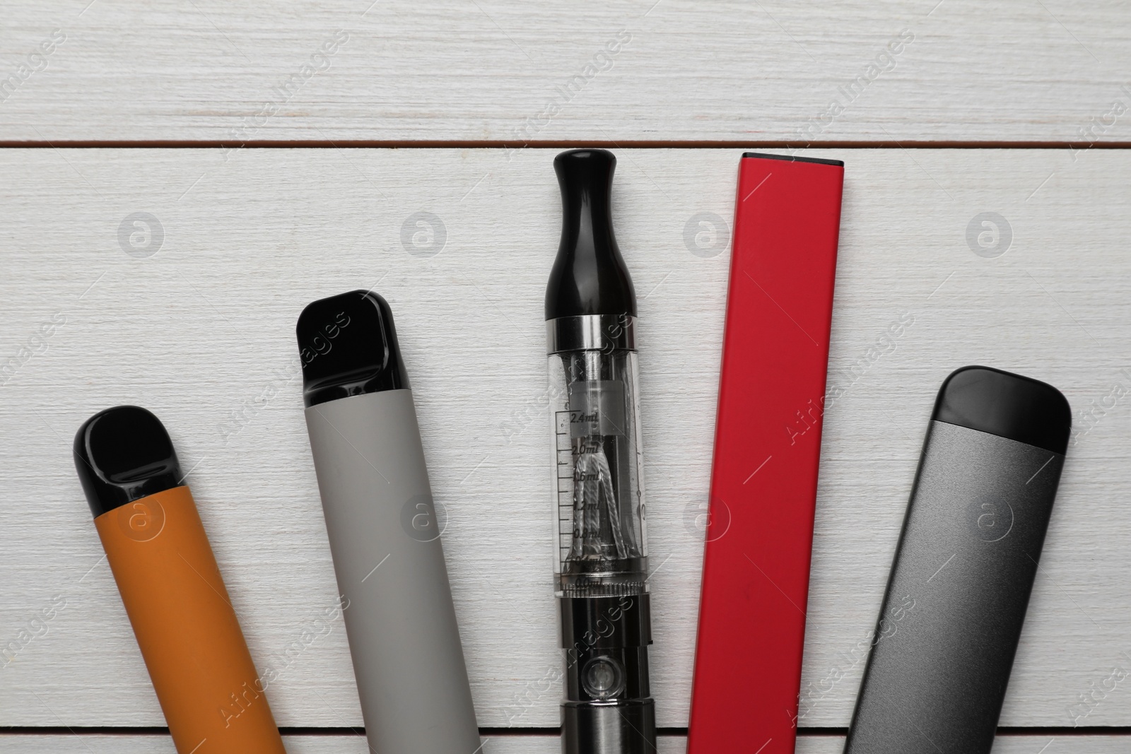 Photo of Different electronic cigarettes on white wooden background, flat lay