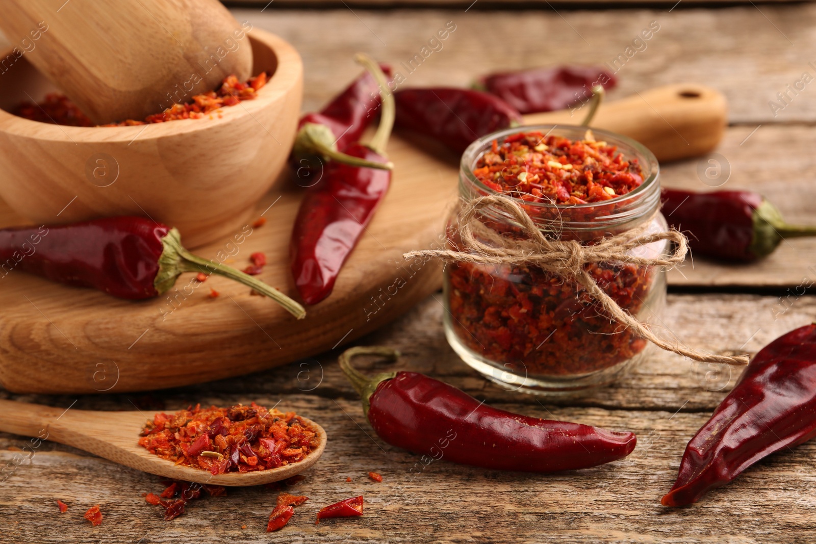 Photo of Chili pepper flakes and pods on wooden table