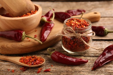 Photo of Chili pepper flakes and pods on wooden table