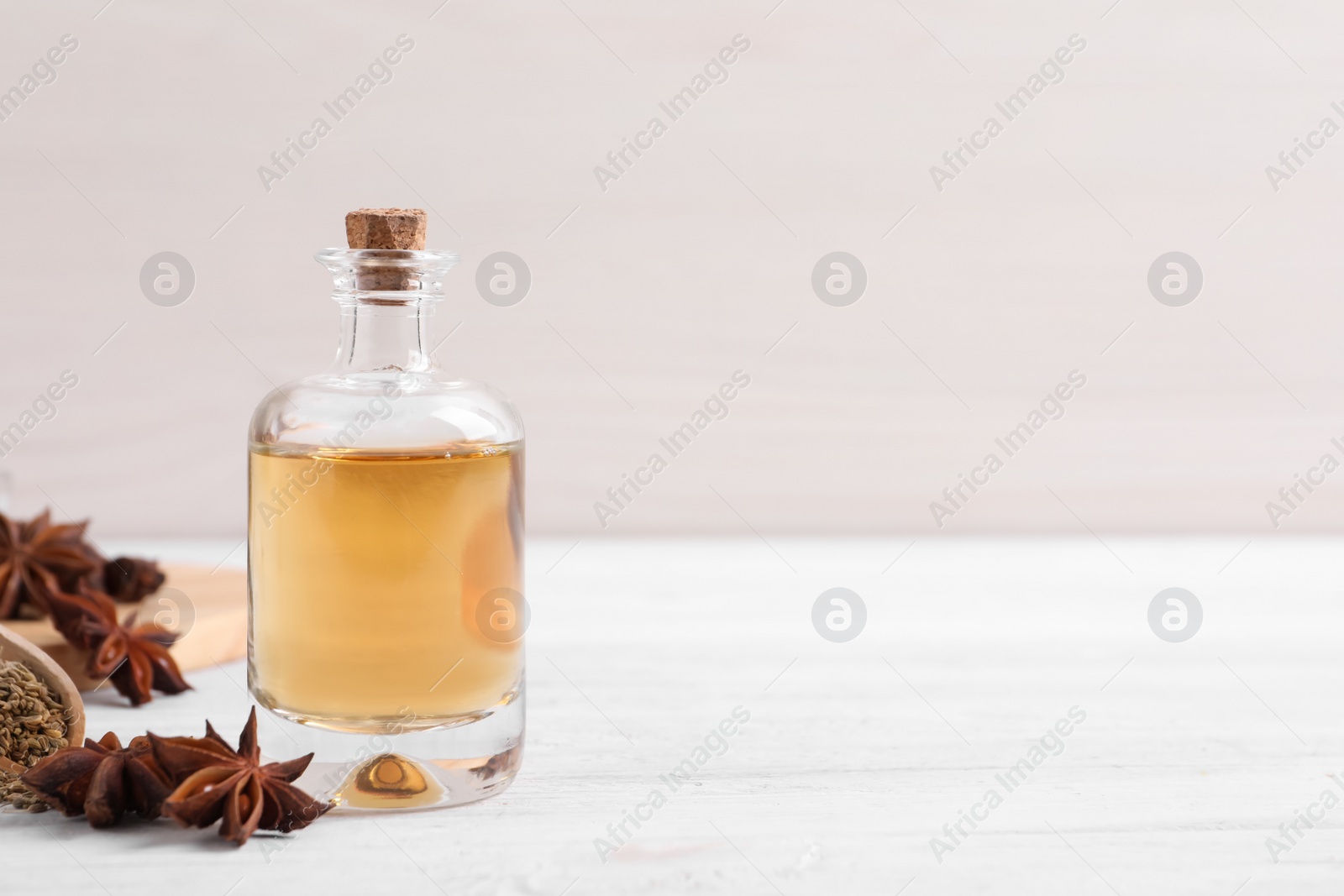 Photo of Bottle of essential oil, anise and seeds on white wooden table. Space for text