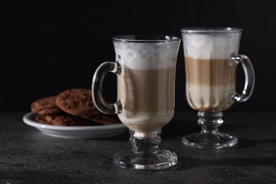 Photo of Aromatic latte macchiato in glasses and chocolate cookies on dark grey table