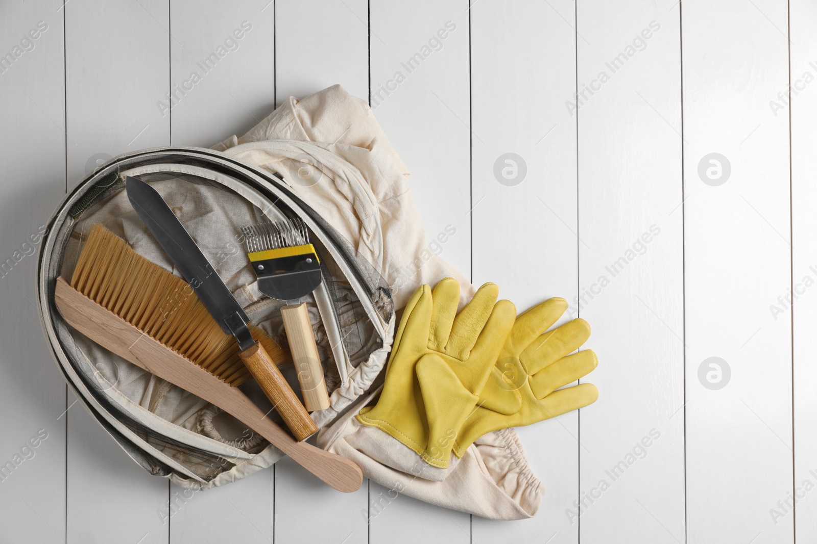 Photo of Different beekeeping tools on white wooden table, flat lay. Space for text