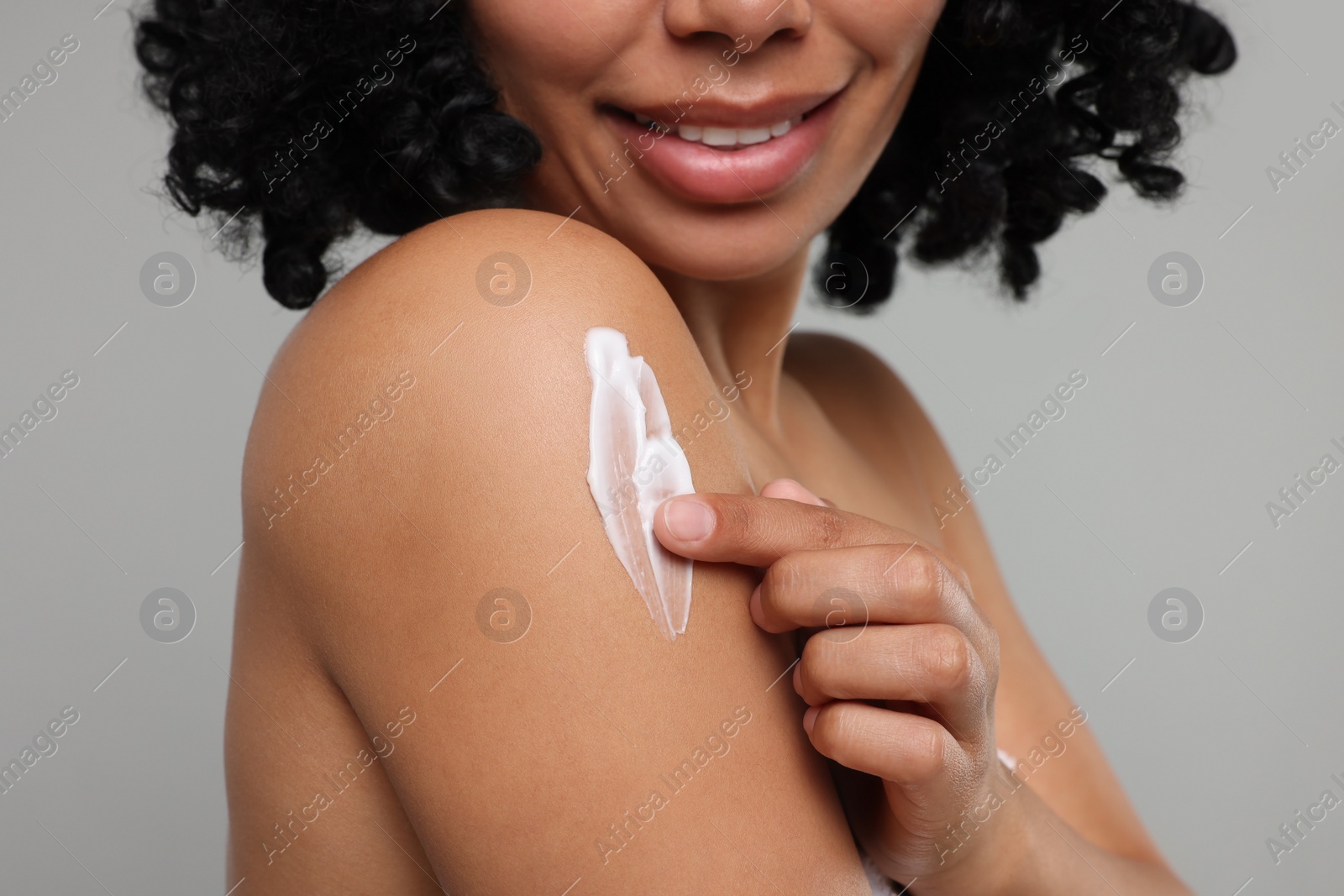 Photo of Young woman applying body cream onto shoulder on grey background, closeup