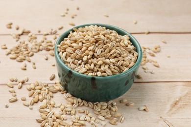 Photo of Dry pearl barley in bowl on light wooden table, closeup